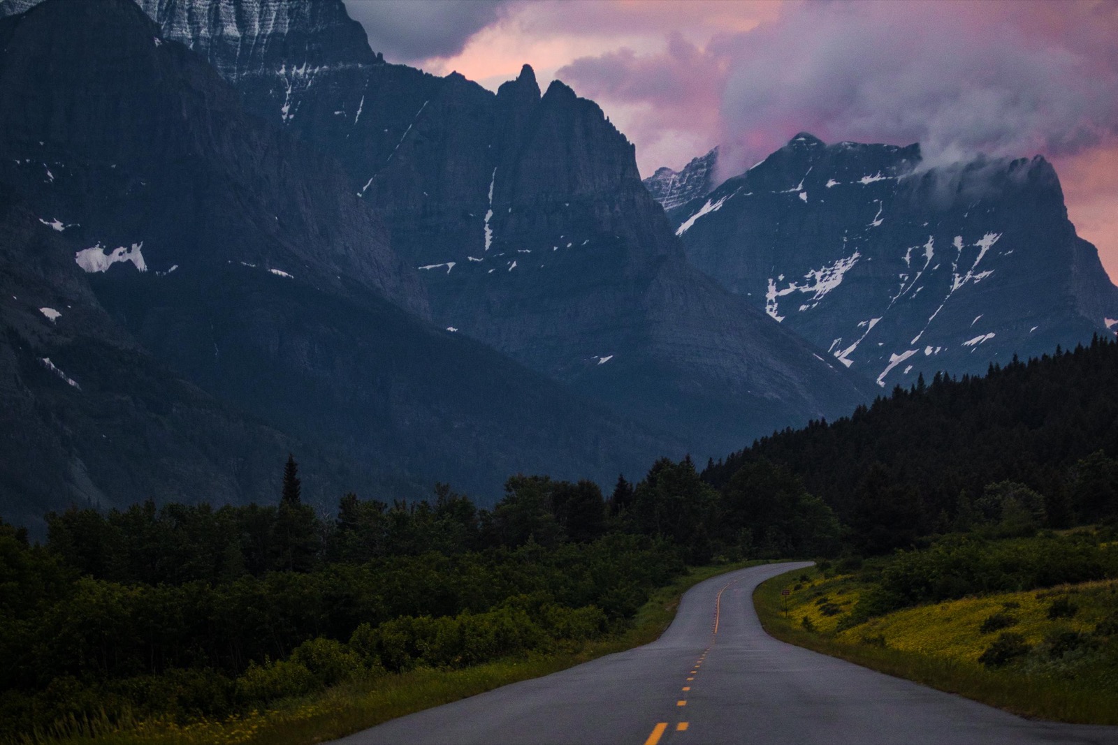 Going-to-the-Sun Road winding through a forested valley below jagged peaks at Glacier National Park, Montana